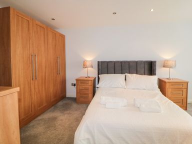A bedroom with a double bed with white bedding two wooden nightstands with lamps and a large wooden wardrobe at Fonthill in Torquay