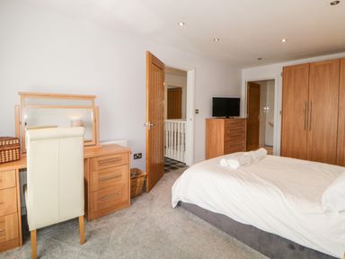A bedroom with a bed with rolled towels a dresser with a tv a wardrobe a dressing table with a chair and an open door at Fonthill in Torquay