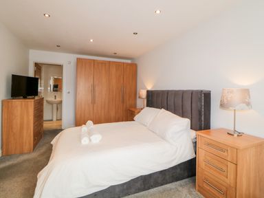 A bedroom with a bed towels on top a bedside table with lamp a wooden wardrobe and a dresser with a television at Fonthill in Torquay