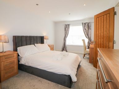 A bedroom with a double bed a window with curtains bedside tables with lamps a wooden door and a dresser at Fonthill in Torquay