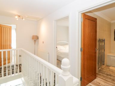 A hallway with white railing and three wooden doors leading to a bedroom and bathroom at Fonthill in Torquay