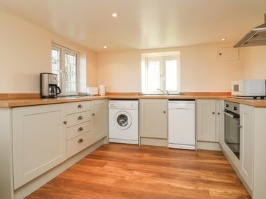 A kitchen with wooden floors appliances and two windows at The Linhay in Holsworthy