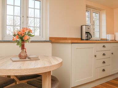 A kitchen with a round wooden table with flowers in a vase and cabinets with a coffee maker at The Linhay in Holsworthy