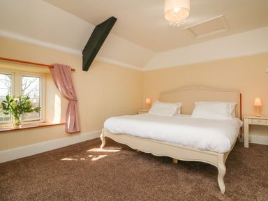 A bedroom with a bed two bedside tables two lamps a window with curtains and a vase of flowers at The Linhay in Holsworthy