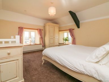 A bedroom with a bed dresser wardrobe two windows with pink curtains and a ceiling light at The Linhay in Holsworthy
