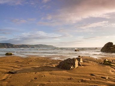 A sandy beach with rocks and waves under a cloudy sky at The Linhay in Holsworthy
