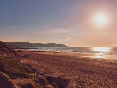 A beach with people walking near the water and rocky cliffs in the background at The Linhay in Holsworthy