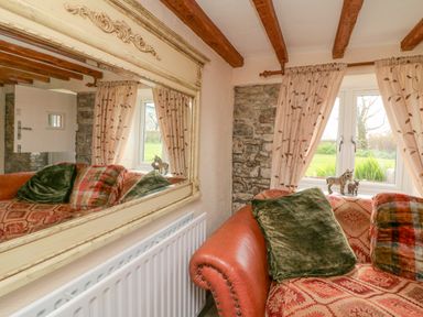 A corner of a room with a patterned sofa cushions window with curtains a radiator and a large ornate mirror on the wall at The Linhay in Holsworthy