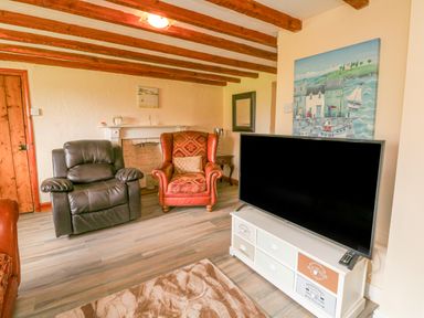 A living room with wooden beams leather and fabric armchairs a flat screen tv on a stand and a painting on the wall at The Linhay in Holsworthy
