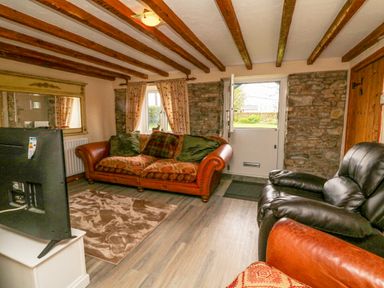 A living room with a leather sofa armchair a television a mirror and exposed wooden beams at The Linhay in Holsworthy