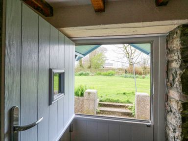 An open wooden door and window looking out to a garden with grass stone steps and a fence at The Linhay in Holsworthy