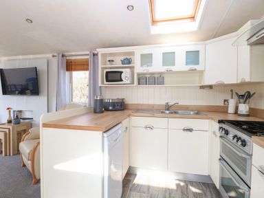 A kitchen with white cabinets a sink a microwave a stove and a dishwasher next to a living area at 109 Pentney Lakes in Pentney near King's Lynn
