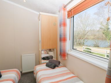 A small bedroom with two single beds a wardrobe and a window overlooking trees and water at 109 Pentney Lakes in Pentney near Kings Lynn