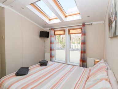 A bedroom with a double bed striped bedding skylights and a wall-mounted TV at 109 Pentney Lakes Pentney near King's Lynn