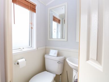 A small bathroom with a toilet a sink a wall mirror and a window with wooden blinds at 109 Pentney Lakes Pentney near King's Lynn