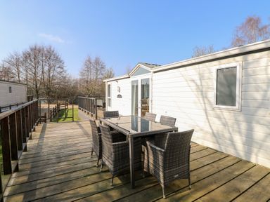 An outdoor wooden deck with a glass top table and six wicker chairs next to a white mobile home at 109 Pentney Lakes in Pentney near King's Lynn