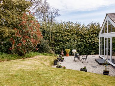 A garden area with patio furniture and potted plants next to a glass conservatory at The Old Vicarage Retreat in Luxulyan