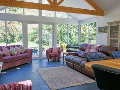 A living room with sofas armchairs a dining table and large windows at The Old Vicarage Retreat Luxulyan