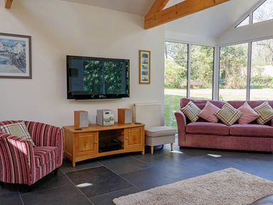 A living room with a pink sofa and striped armchair a wooden TV stand with a stereo and a wall mounted TV at The Old Vicarage Retreat in Luxulyan