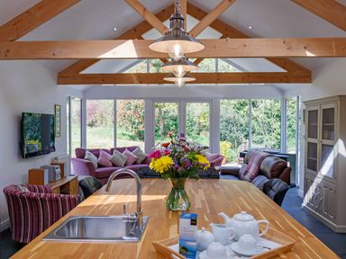 A kitchen island with a sink and flowers with a living area including sofas and a TV at The Old Vicarage Retreat in Luxulyan