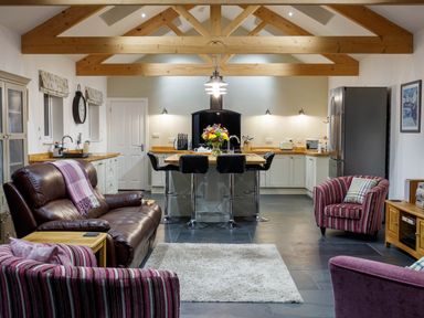 A kitchen and living area with exposed wooden beams a brown leather sofa striped armchairs a kitchen island with bar stools and a refrigerator at The Old Vicarage Retreat in Luxulyan