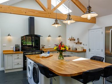 A kitchen with a wooden island countertop seating black chairs a stove and a refrigerator at The Old Vicarage Retreat in Luxulyan