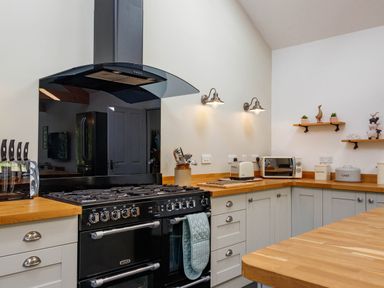 A kitchen with a black oven and stove a knife set toaster microwave and shelves with decorations at The Old Vicarage Retreat in Luxulyan