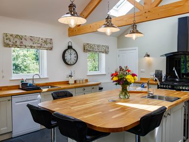 A kitchen with wooden countertops a large island with flowers black chairs and pendant lights at The Old Vicarage Retreat in Luxulyan