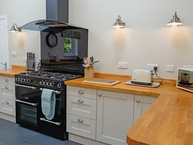 A kitchen with a black stove, wooden countertops, white cabinets, a toaster, a microwave, and wall lights at The Old Vicarage Retreat in Luxulyan