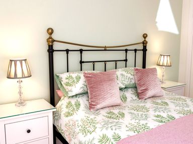 A bedroom with a black metal bed frame white bedside tables with lamps and floral bedding at The Old Vicarage Retreat in Luxulyan