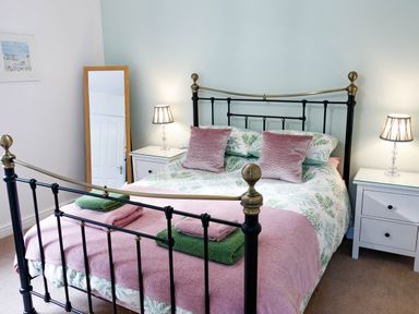 A bedroom with a metal bed frame pink and green bedding bedside tables with lamps and a standing mirror at The Old Vicarage Retreat in Luxulyan