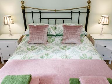 A bedroom with a bed with leafy bedding two pink pillows two bedside tables and lamps at The Old Vicarage Retreat in Luxulyan