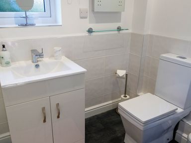 A bathroom with a white sink cabinet a toilet and a window at The Old Vicarage Retreat in Luxulyan