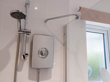 A showerhead and electric shower unit with a glass shower screen and frosted window in a bathroom at The Old Vicarage Retreat in Luxulyan