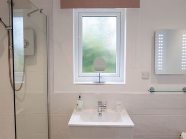 A bathroom with a sink, a window with frosted glass, a small mirror, and a shower area at The Old Vicarage Retreat in Luxulyan