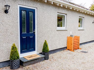 Exterior of a building with a blue door a welcome mat two potted plants and two windows at The Old Vicarage Retreat in Luxulyan