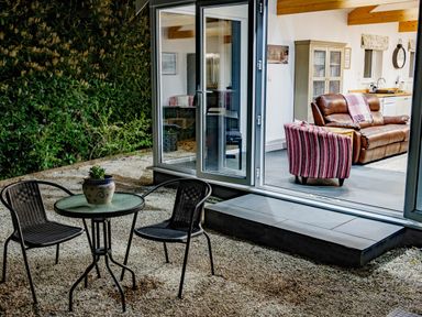 An outdoor seating area with two chairs and a round table with a plant next to a room with leather sofa and striped armchair at The Old Vicarage Retreat in Luxulyan