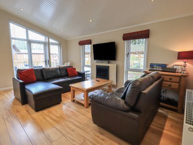 A living room with two black leather sofas a wooden coffee table and a wall mounted tv at Oakwood Lodge in Langdale 3 White Cross Bay Windermere
