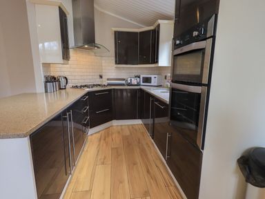 A kitchen with dark cabinets beige countertops wood flooring and stainless steel appliances at Oakwood Lodge Langdale 3 White Cross Bay Windermere