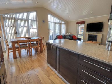 An open plan room with a wooden dining table and chairs a kitchen island with countertop a sofa with red cushions and a wall-mounted television at Oakwood Lodge Langdale 3 White Cross Bay Windermere