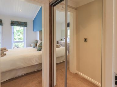A bedroom with a bed and pillows visible through a doorway and a mirrored closet door in a hallway at Oakwood Lodge in Langdale 3 White Cross Bay Windermere