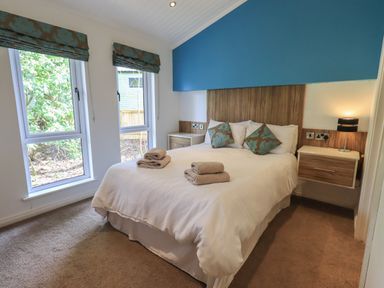 A bedroom with a double bed two bedside tables a lamp and two windows at Oakwood Lodge in Langdale 3 White Cross Bay Windermere