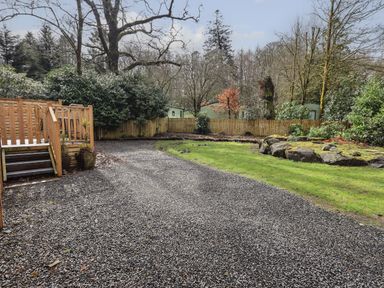 A backyard with a gravel path wooden stairs grassy area rocks and trees at Oakwood Lodge in Langdale 3 White Cross Bay Windermere