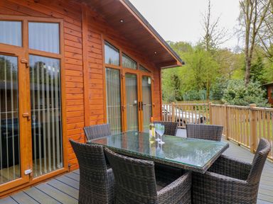 An outdoor deck with a glass table and wicker chairs outside a wooden cabin at Oakwood Lodge Langdale 3 White Cross Bay Windermere
