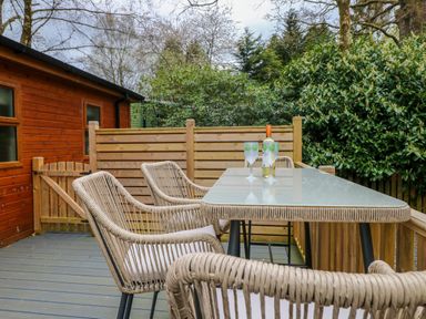 An outdoor patio with a glass table and wicker chairs next to a wooden building at Oakwood Lodge Langdale 3 White Cross Bay Windermere