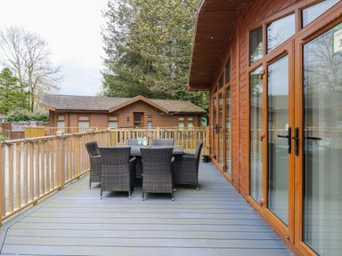 An outdoor deck with a table and six chairs next to a wooden lodge at Oakwood Lodge in Langdale 3 White Cross Bay Windermere