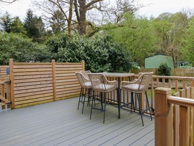 An outdoor deck with a table and four chairs surrounded by wooden fencing and trees at Oakwood Lodge in Langdale 3 White Cross Bay Windermere
