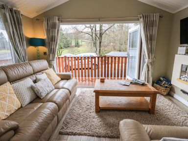 A living room with a leather sofa cushions coffee table rug and glass door opening to a balcony at Lakeland View Lodge Beckside 2 Limefitt Park near Windermere