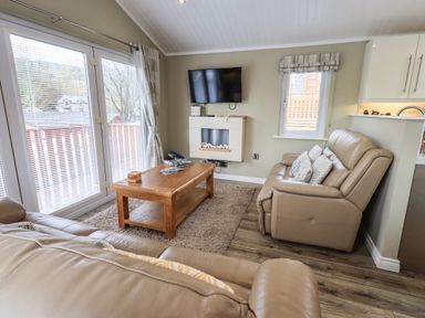 A living room with beige leather sofas a wooden coffee table a wall-mounted TV and large windows at Lakeland View Lodge Beckside 2 Limefitt Park near Windermere