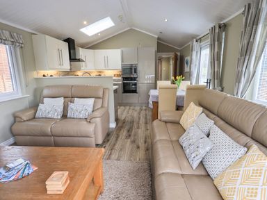 A living room with two leather sofas and a wooden coffee table next to a dining area and kitchen at Lakeland View Lodge in Beckside 2 Limefitt Park near Windermere